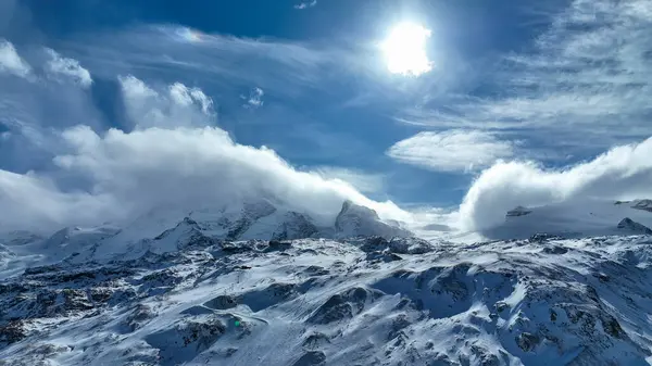 İsviçre 'deki Zermatt kayak merkezinin manzarasında açık mavi gökyüzü altında Matterhorn, kayak asansörleri, karla kaplı yamaçlar ve engebeli alp zirveleri görülüyor..