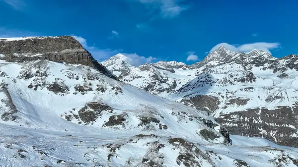 Görkemli kar tepeli dağ zirvesi berrak mavi gökyüzüne karşı dimdik duruyor. Kış manzarasının engebeli güzelliğini gözler önüne seriyor..