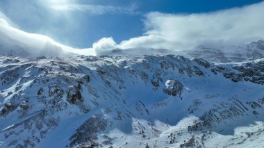 Kar kaplı kaya dağları gökyüzünün altında hafif bulutlarla zirve yapıyor..