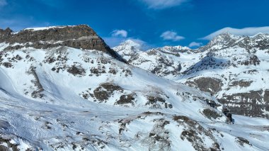 Görkemli kar tepeli dağ zirvesi berrak mavi gökyüzüne karşı dimdik duruyor. Kış manzarasının engebeli güzelliğini gözler önüne seriyor..