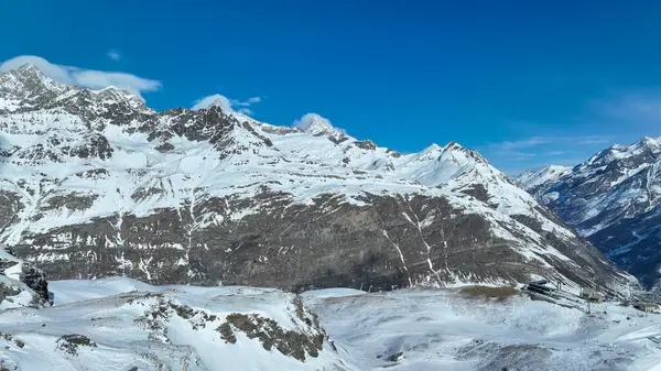 Görkemli kar tepeli dağ zirvesi berrak mavi gökyüzüne karşı dimdik duruyor. Kış manzarasının engebeli güzelliğini gözler önüne seriyor..