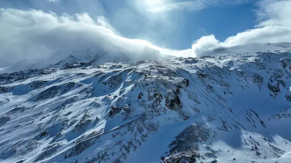 Kar kaplı kaya dağları gökyüzünün altında hafif bulutlarla zirve yapıyor..