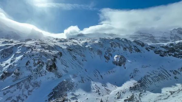 Kar kaplı kaya dağları gökyüzünün altında hafif bulutlarla zirve yapıyor..