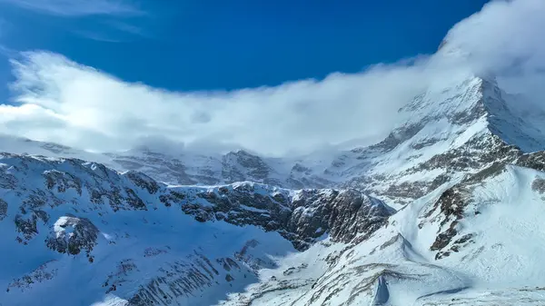 İsviçre Alplerinde bulutların ve mavi gökyüzünün altında görkemli karlı dağ zirvesi.
