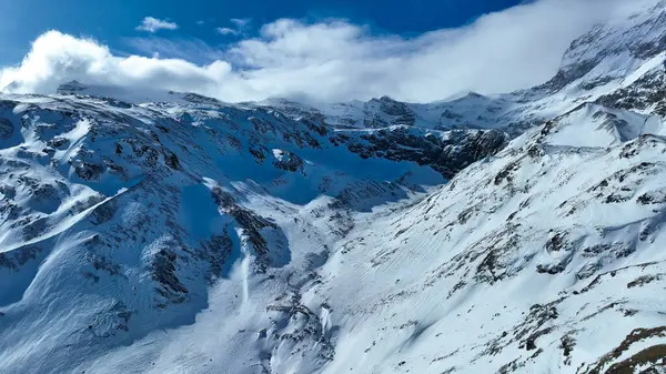 Karlı bir dağ zirvesinden nefes kesici bir manzara. Geniş kış manzaralarına bakan bir kayak kaldırma yapısına sahip, engebeli tepeler ve dramatik bulutlu bir gökyüzünün altında uzak tepeler..