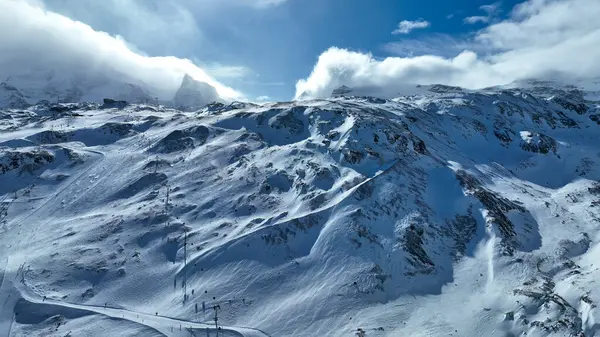 Karlı bir dağ zirvesinden nefes kesici bir manzara. Geniş kış manzaralarına bakan bir kayak kaldırma yapısına sahip, engebeli tepeler ve dramatik bulutlu bir gökyüzünün altında uzak tepeler..
