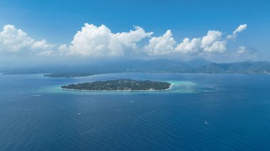 Lombok adasının arka planında bulutlar olan Gili Hava Adası 'nın insansız hava aracı görüntüsü. Lombok 'a bakan Gili Air manzaralı sisli dağlar ve sakin deniz manzarası.