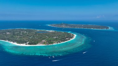 Mavi bir okyanusta Gili Meno adasını geçen küçük bir teknenin havadan görünüşü.