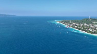 Tropik beyaz kumsal arka planı. Gök mavisi deniz suyu, küçük dalgalar ve mercan resifi. Gili Trawangan ve Gili Meno adaları arasında giden tekneler.