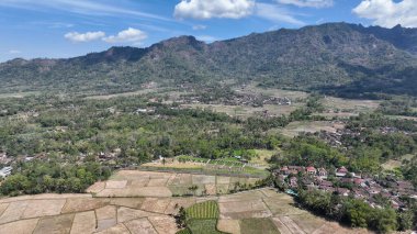 Görkemli hava manzarası, engin tarlaları, huzurlu bir köyü ve berrak mavi gökyüzünün altındaki volkanik dağların dramatik zeminini yakalıyor..