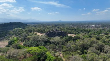 İkonik Borobudur, Endonezya 'nın zengin mirasının zamansız bir sembolü olan sık orman ve uzak dağlarla çevrili ağaç tepelerinin üzerinde yükselir..