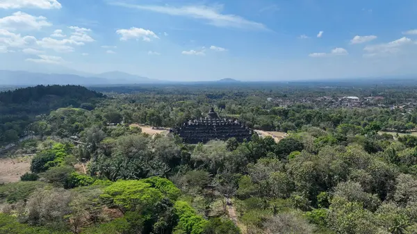 İkonik Borobudur, Endonezya 'nın zengin mirasının zamansız bir sembolü olan sık orman ve uzak dağlarla çevrili ağaç tepelerinin üzerinde yükselir..