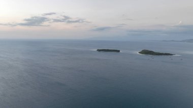 Alacakaranlıkta sakin mavi denizle çevrili Gili adalarının hava manzarası. Sakin sahne, bu tropik Endonezya mücevherlerinin uzak güzelliklerini yakalıyor..