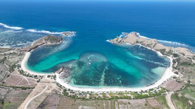 Lombok 'taki hilal şeklinde bir körfezin panoramik görüntüsü. Zümrüt sularının el değmemiş plajlarla buluştuğu ve geniş bir gökyüzünün altında yuvarlanan tepeler..