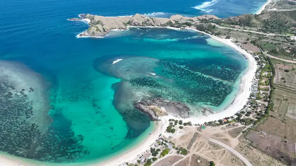Lombok 'ta beyaz kumlu ve kayalık burunlu bir turkuaz körfezin havadan görünüşü. Kristal berrak su yüzeyin altında canlı mercan desenleri gösterir..