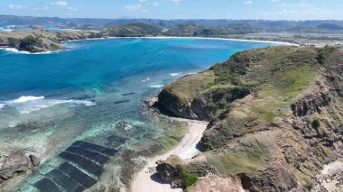 Lombok yakınlarındaki turkuaz su ve dramatik uçurumların havadan görüntüsü. Dikdörtgen yosun çiftlikleri kristal berrak sahil ve beyaz kumlu sahil boyunca çarpıcı bir desen oluşturur..