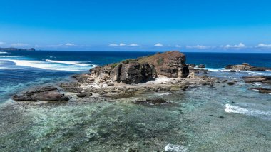 Kayalık mercan resiflerinden yükselir, dalgalar kopar ve okyanus, parlak tropikal güneşin altında dramatik sahil kayalıklarıyla buluşur..