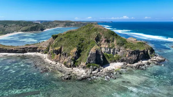 Dik yeşil tepeler kayalık bir kıyı şeridinin üzerinde yükselir, nazik dalgaların kıyıya vurduğu ve denizin sonsuz mavi tonlarda parıldadığı yerde