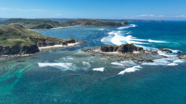 Dramatik uçurumlar, turkuaz su ve geometrik yosun çiftlikleriyle Lombok sahilinin havadan görünüşü dalgaların ve mavi gökyüzünün altında eşsiz bir şablon oluşturuyor..