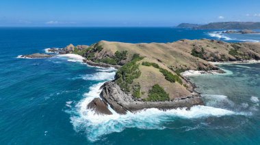 Peninsula 'nın kıyısındaki kayalık kayalıklara ve köpüklü sörflere yakın çekim. Canlı turkuaz deniz, üzerinde engebeli taşlar ve otlak yamaçlarla tezat oluşturuyor..