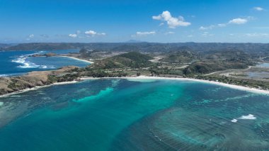 Turkuaz su ve Lombok sahili boyunca beyaz kumsallar kıvrılır. Yuvarlanan tepeler ve dolambaçlı yollar tropikal bir gökyüzünün altında iç kesimlere uzanır..