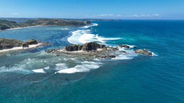 Lombok 'ta engebeli bir kıyı şeridi boyunca kristal mavi dalgalar koparken tropikal güneşin altında sonsuz sayıda yosun tarlası yüzeyin altında parıldıyor..