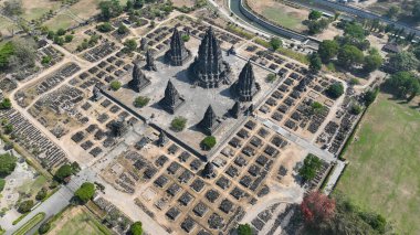Prambanan Tapınağı, daha küçük tapınakların düzenli kalıntıları ve yakındaki nehrin nazik kıvrımları tarafından çerçevelenmiş karmaşık taş kuleleri ile sahneye hükmediyor..