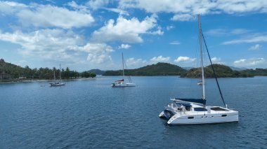 Katamaranlar ve yelkenliler, küçük tropik adalar ve palmiye kaplı plajlar tarafından çerçevelenmiş sakin bir lagüne demirlediler. Mavi gökyüzü ve yumuşak dalgalar rüya gibi bir ada havası yaratır..
