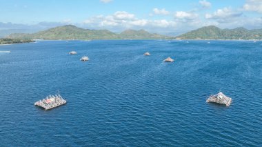 Geleneksel bambu balıkçılık platformları arka planda yeşil dağlarla açık denizde yüzerler. Bu benzersiz sahne ada yaşamının ruhunu yakalar..