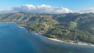 Lombok adasındaki sakin bir sahil köyünün havadan görünüşü. Turkuaz denizin dramatik bir gökyüzü altında yemyeşil tepelerle buluştuğu yer. Doğa ve macera aşıkları için mükemmel..
