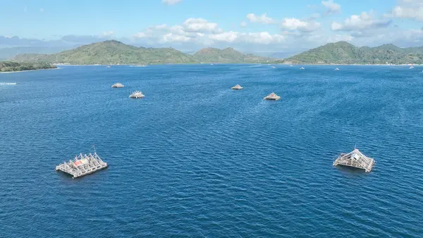 Geleneksel bambu balıkçılık platformları arka planda yeşil dağlarla açık denizde yüzerler. Bu benzersiz sahne ada yaşamının ruhunu yakalar..