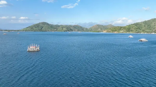 Sakin bir körfezin manzarası bambu balıkçı sallarıyla kaplı, yeşil tepeler ve berrak bir gökyüzünün altında huzurlu bir kıyı şeridi ile çevrili..