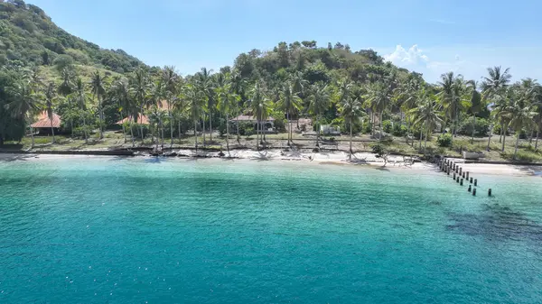 Palmiye ağaçları, berrak su ve yeşil bir yamacın eteğinde yuva yapmış kırsal kır evleriyle huzurlu bir kıyı şeridi oluşturarak sakin bir tropikal kaçış sağlar..
