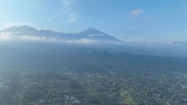 Sonu gelmeyen yeşil manzaralar ve huzur dolu köyler aşağıda sergilenirken, güçlü volkan Rinjani kuleleri arka planda, zirvesi mistik sabah sisi ile örtülüydü..
