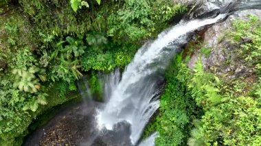 Tiu Kelep şelalesinin hava perspektifi, nehrin kayaların arasından geçerek yeşilliğe gizlenmiş sisli bir havuza düştüğünü gösteriyor..