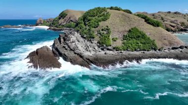 Peninsula 'nın kıyısındaki kayalık kayalıklara ve köpüklü sörflere yakın çekim. Canlı turkuaz deniz, üzerinde engebeli taşlar ve otlak yamaçlarla tezat oluşturuyor..