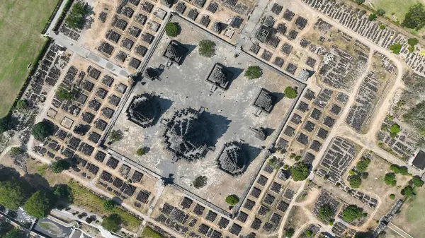 Nefes kesici bir hava manzarası, Java 'da dağınık taş kalıntıları ve yemyeşil ağaçlarla çevrili antik bir tapınak kompleksinin karmaşık planını ortaya koyuyor..