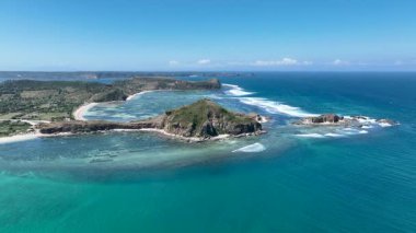 Dramatik uçurumlar, turkuaz su ve geometrik yosun çiftlikleriyle Lombok sahilinin havadan görünüşü dalgaların ve mavi gökyüzünün altında eşsiz bir şablon oluşturuyor..