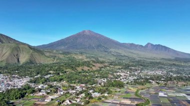Sembalun 'un görkemli yamaçları Rinjani Dağı' nın altına yayılarak, tropikal güneşin altında kayan tepelerden ve volkanik araziden oluşan dramatik bir manzara yarattı..