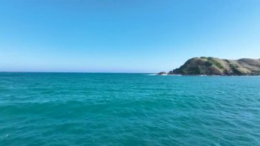 Çarpıcı bir sahil kayalığı, dingin denizle buluşan parlak beyaz kayalıkları gösteriyor. Canlı yeşillik ve dağınık çiçekler derin mavi sulara ve açık gökyüzüne zıtlık ekler..