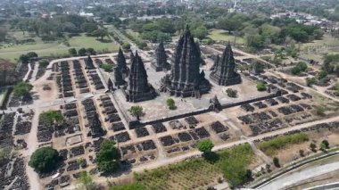Görkemli Prambanan kompleksi engin bir arkeolojik alanın kalbinde duruyor, ikonik kuleleri gökyüzüne doğru uzanıyor dağınık tapınak kalıntıları ve yemyeşil alanlar arasında...