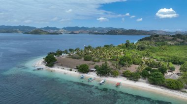 Hindistan cevizi palmiyeleri, beyaz plajları ve kıyıya demirlemiş renkli tekneleri olan sakin bir tropikal adanın havadan görünüşü. Dağlar, sakin mavi deniz boyunca yükselir..