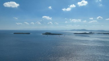 Geleneksel bambu balıkçılık platformları arka planda yeşil dağlarla açık denizde yüzerler. Bu benzersiz sahne ada yaşamının ruhunu yakalar..
