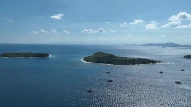 Geleneksel bambu balıkçılık platformları arka planda yeşil dağlarla açık denizde yüzerler. Bu benzersiz sahne ada yaşamının ruhunu yakalar..