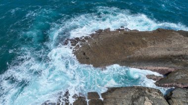 Dalgalar, turkuaz su enerjiyle girdap gibi girdap gibi dönerken engebeli kıyı kayalarına çarpar. Doğa bu dramatik kıyı şeridi boyunca ham gücünü ve güzelliğini sergiliyor..