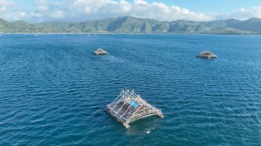 Bambu balıkçılık platformları Lombok yakınlarındaki derin mavi denizi işaret ediyor. Görüntü geometrik şekilleri ve dağlık adaları vurgular..