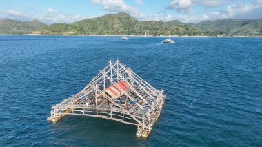 Kırmızı çatılı eşsiz bambu balıkçılık platformu derin mavi denize karşı duruyor. Lombok kıyı şeridine yakın mesafeden buna benzer birkaç sal görülebilir..