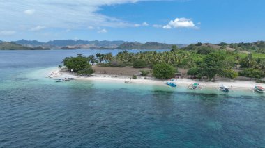 Hindistan cevizi palmiyeleri ve zümrüt sularıyla çevrili beyaz kumu olan sessiz bir adanın çarpıcı manzarası. Renkli tekneler sakin kumsalda, tropikal bir kaçış için mükemmel..