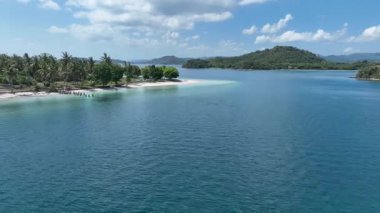 Zümrüt sularının mercan resifleriyle buluştuğu ve palmiye ağaçlarının sahil boyunca yeşil bir vaha oluşturduğu sakin bir ada köşesinin nefes kesici hava perspektifi..