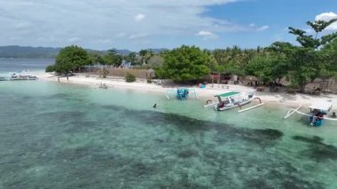 Kristal berrak turkuaz su, geleneksel tekneler ve yemyeşil ağaçlarla benekli beyaz kumlu bir plajla karşılaşıyor. Yüzmek ve rahatlamak için mükemmel bir tropikal kaçış..